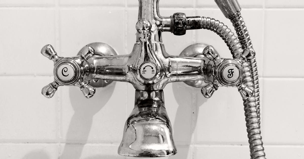 Chrome bathtub faucet with cross handles and a shower hose against white tiled wall