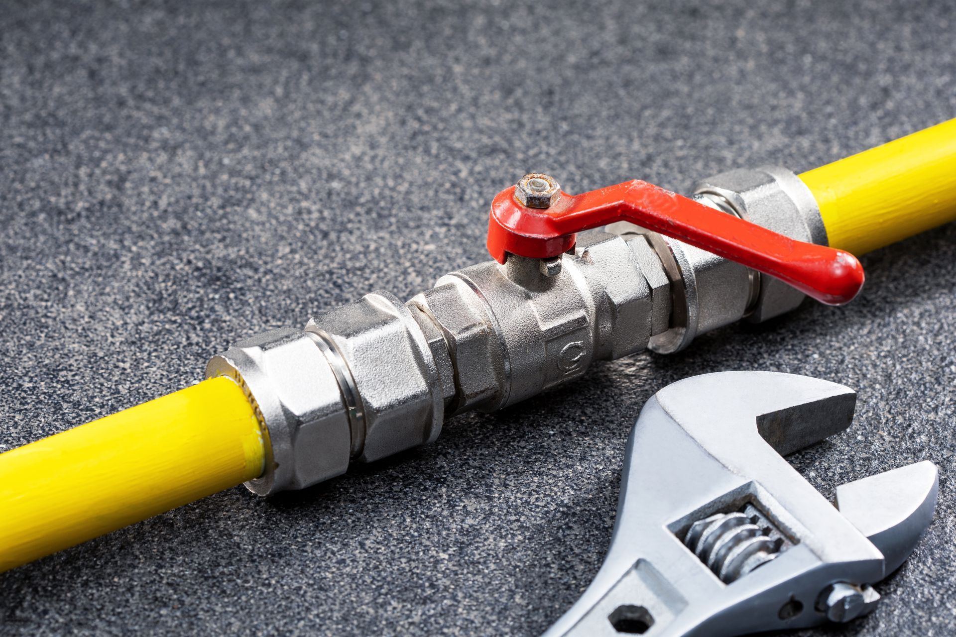 Yellow gas pipe with red shutoff valve and wrench on gray carpet