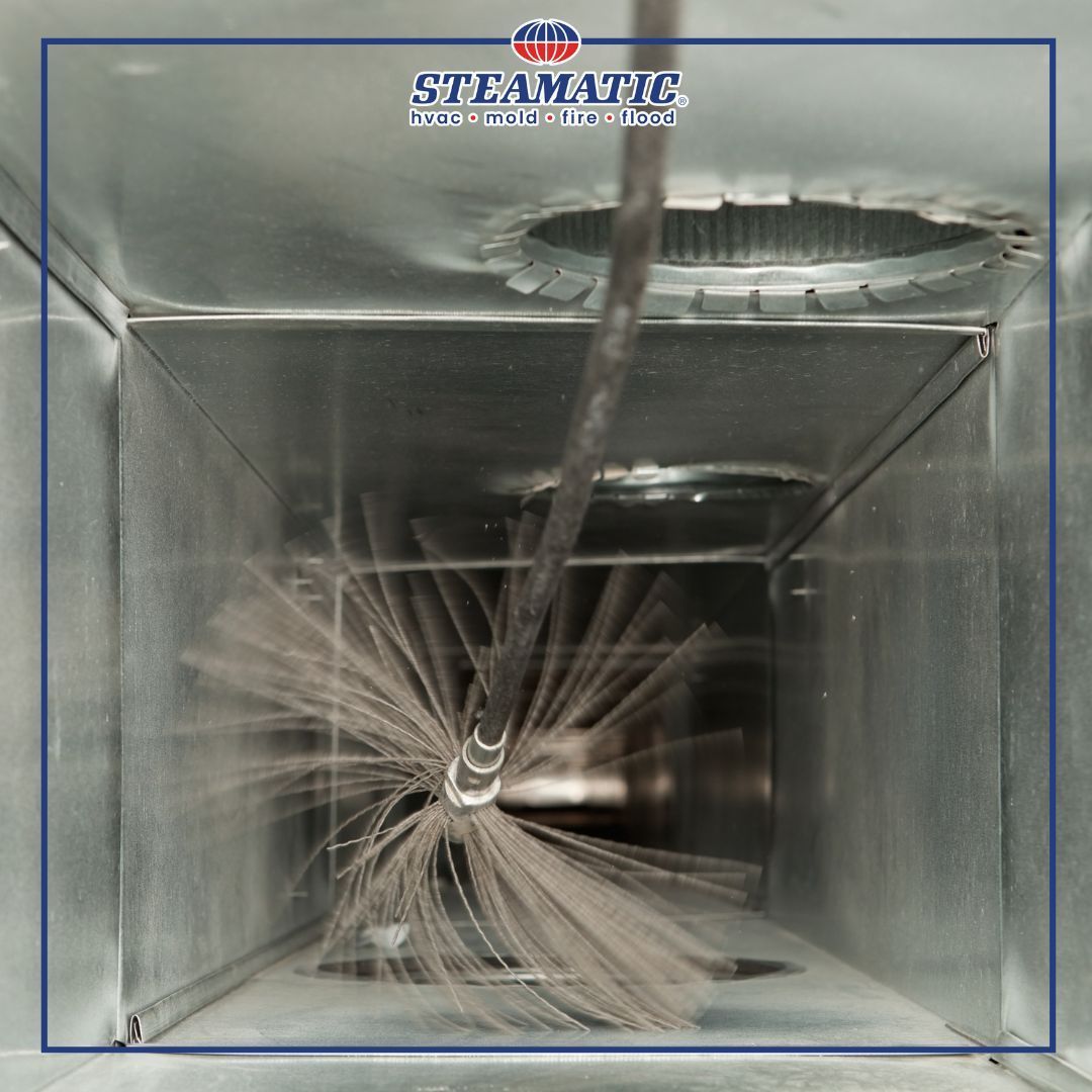 Interior of a duct being cleaned by a spinning brush tool, with gray metal walls and dust buildup.