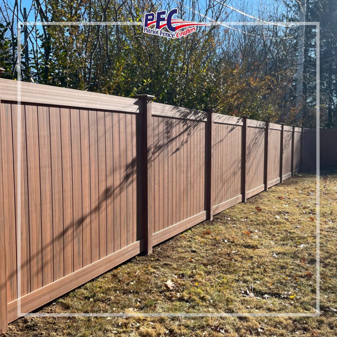 Long brown wooden privacy fence along a grassy yard under trees and blue sky