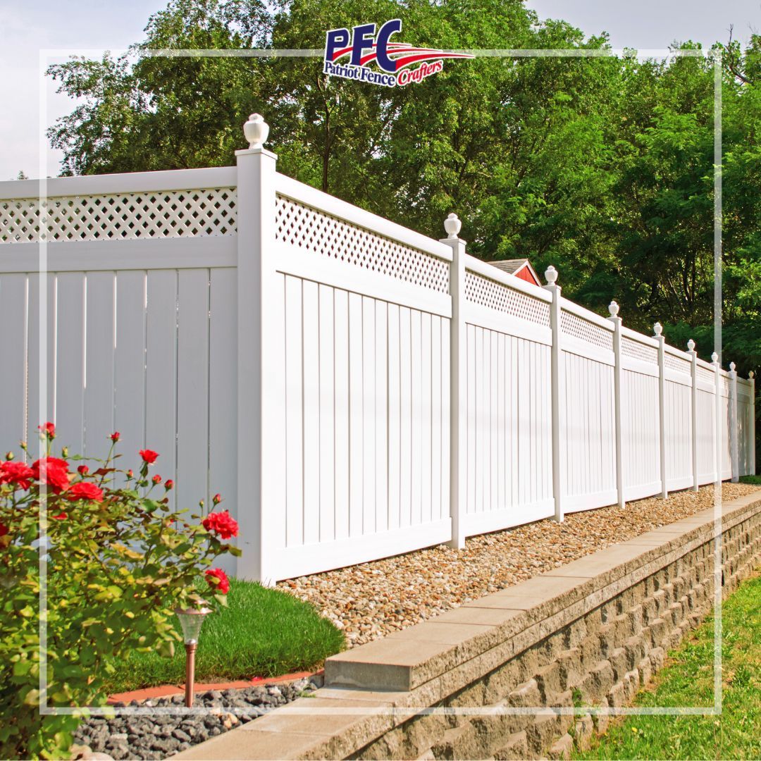 White vinyl privacy fence with lattice top along a stone retaining wall beside a garden with red flowers.