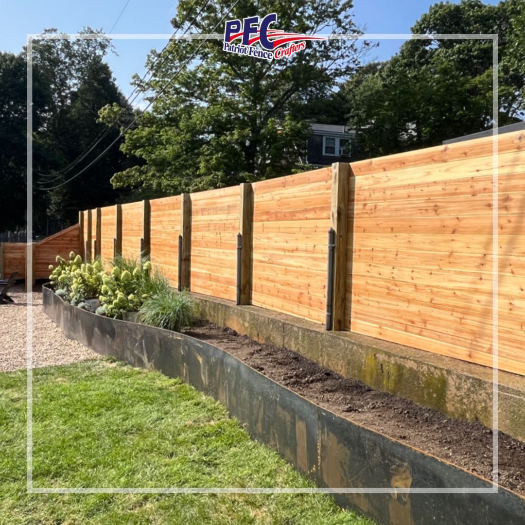Wooden privacy fence along a landscaped retaining wall beside a gravel path and green lawn