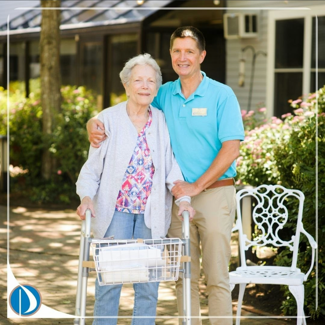 Woman using a walker with a smiling caregiver outdoors by a house