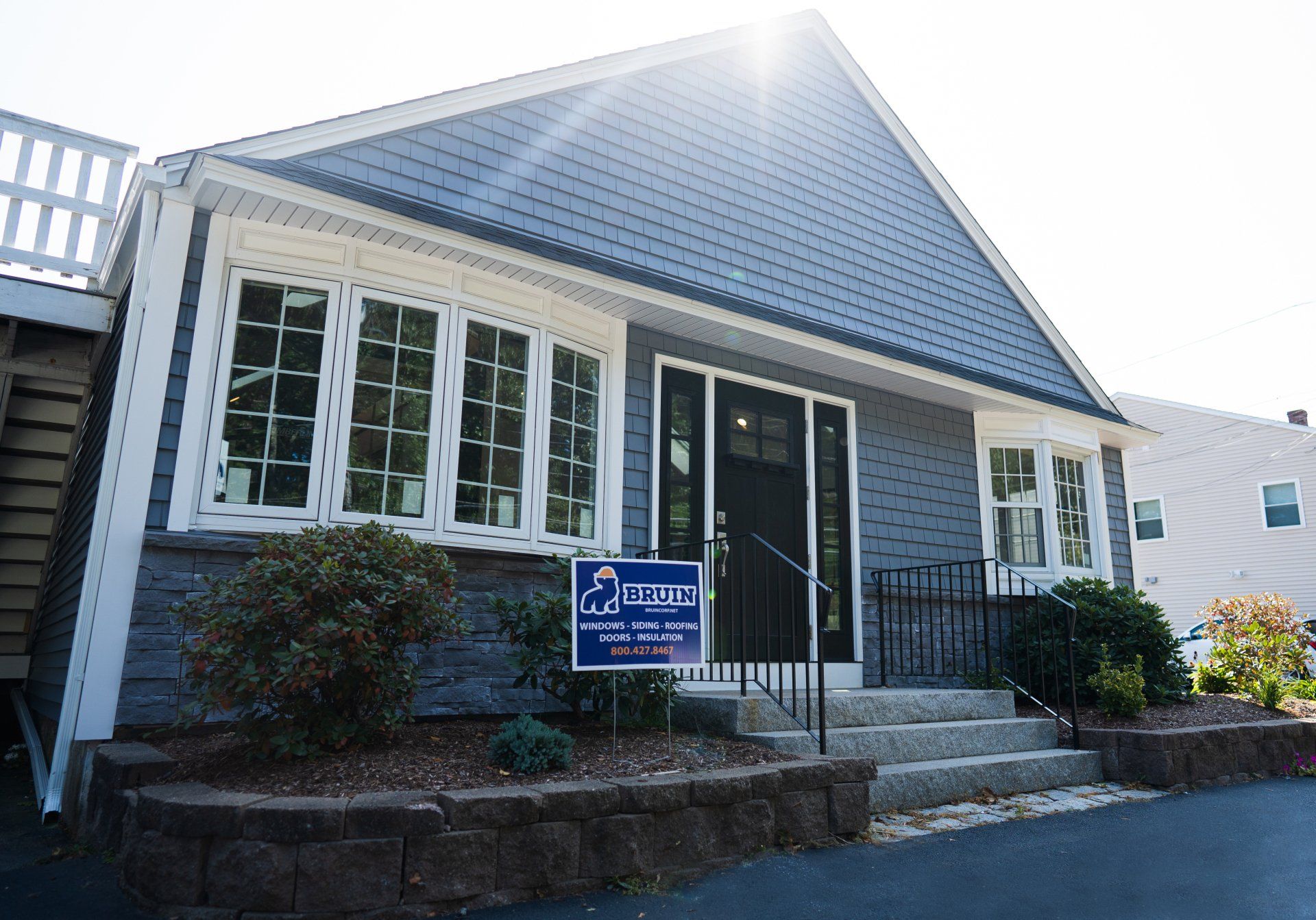 Small white house with black shutters, front steps, and a blue sign by the entrance.