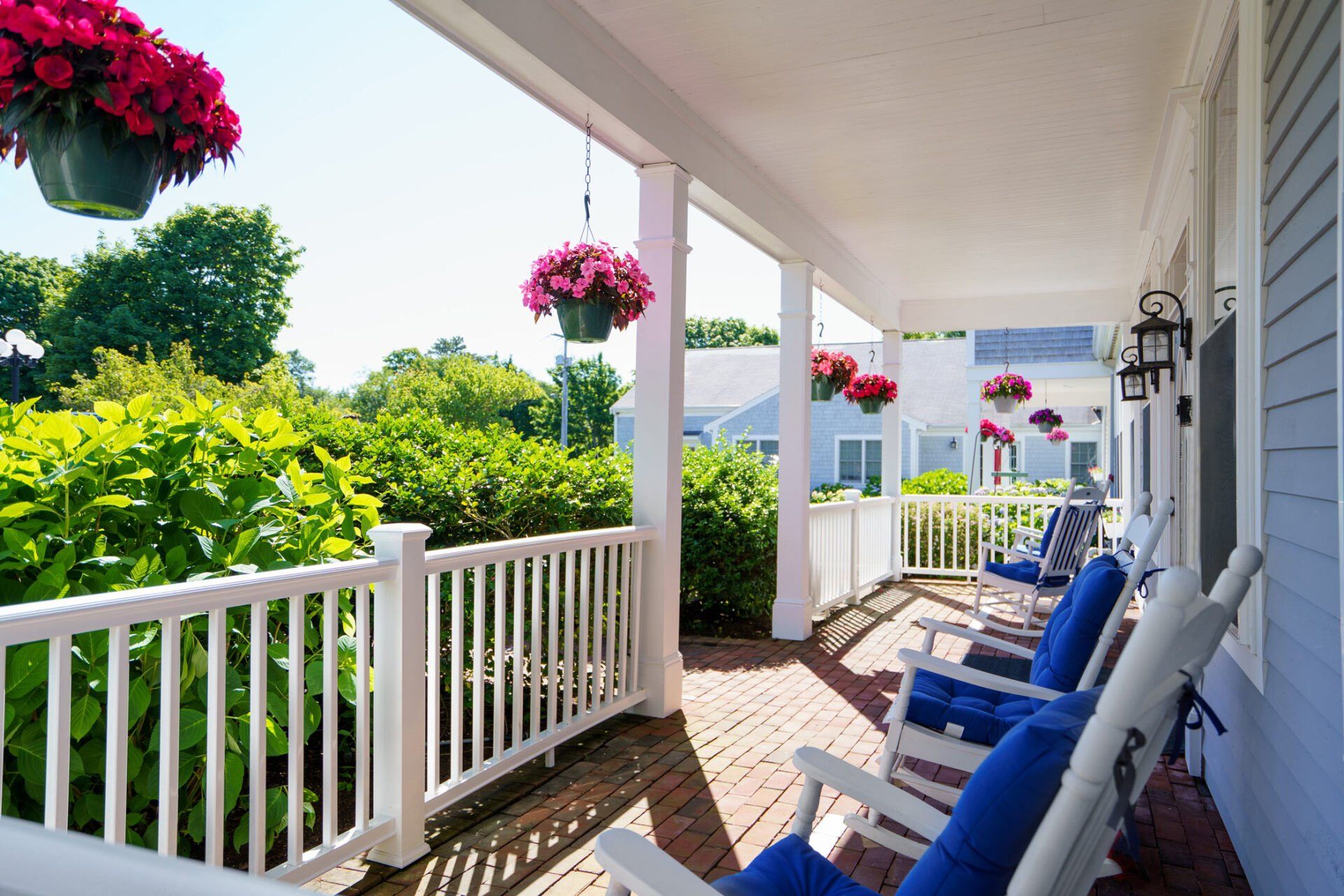 Bright porch with blue chairs, white railing, hanging pink flowers, and greenery in sunlight