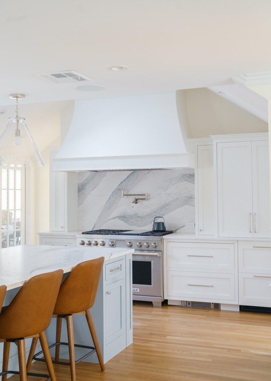 Modern kitchen with white cabinets, marble backsplash, stainless stove, and wood floor beside a breakfast island