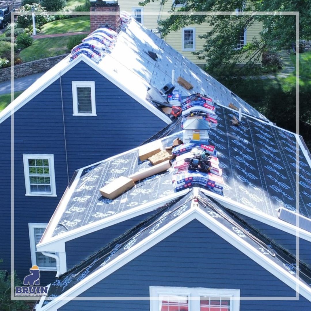 Blue house roof being repaired, with shingles and tools scattered along the peak.