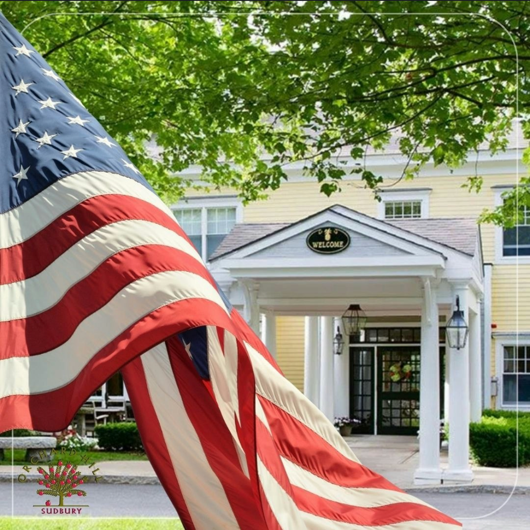 American flag in front of a white colonial-style building with a columned entrance and green trees