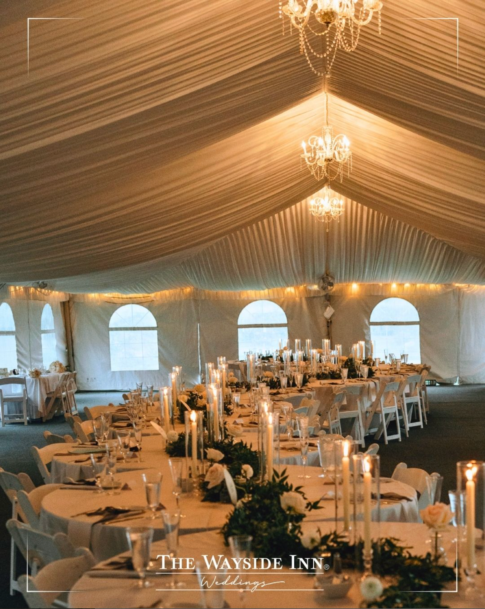 Elegant wedding reception tent with long candlelit tables, chandeliers, and draped ceiling