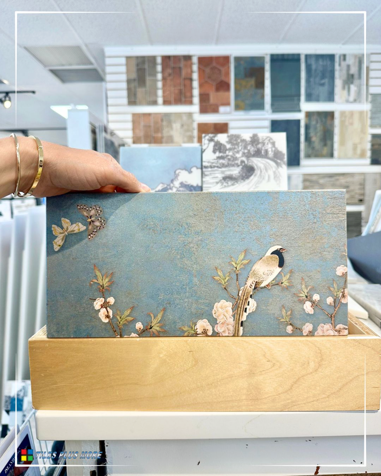 Hand holding a blue floral card in a gold holder, with decorative paper samples in the background