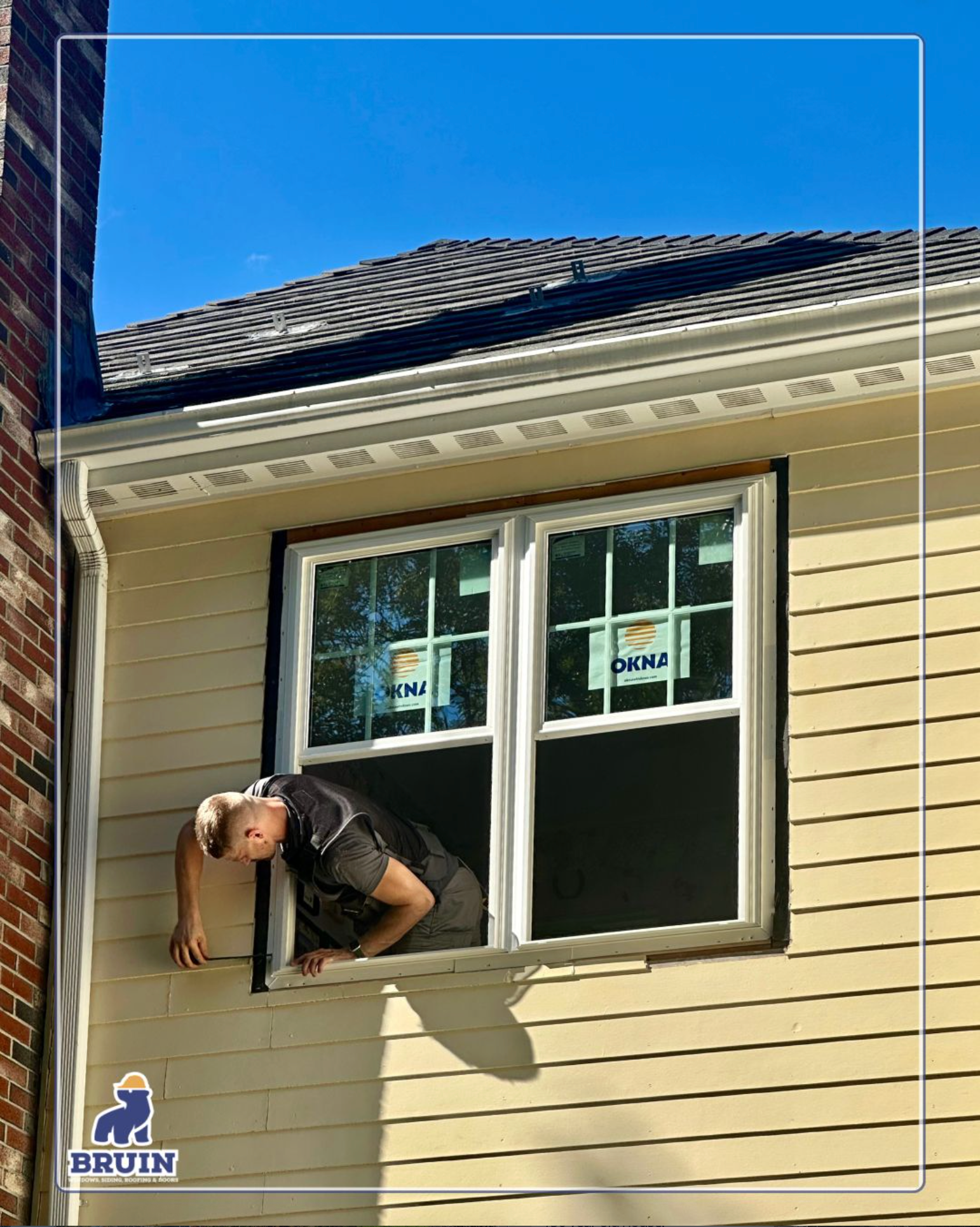 Worker leaning out of a second-story window on a beige house with a blue sky above