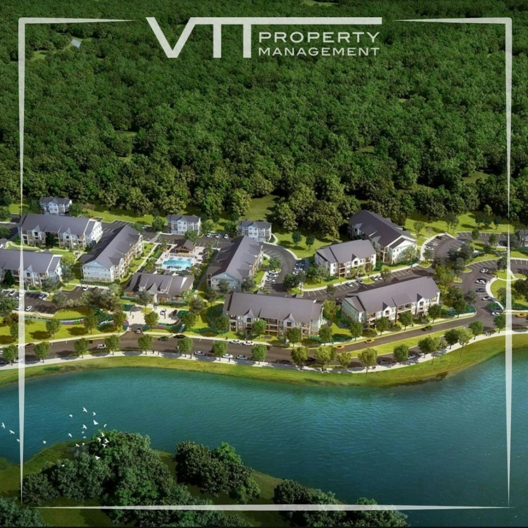 Aerial view of a luxury lakeside property with several homes beside a green forest and blue water, branded VTI Property Management