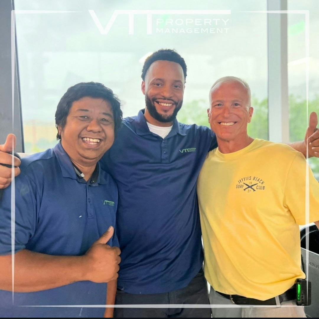 Three smiling people standing together indoors, wearing navy and yellow shirts in front of a glass wall.