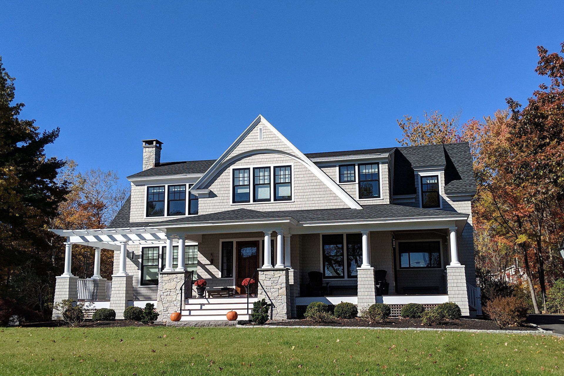White Victorian-style house with a wraparound porch and autumn trees under a clear blue sky