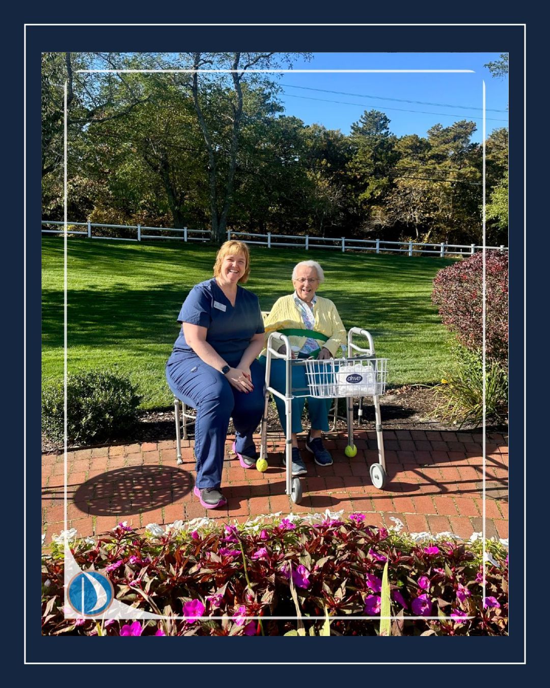 Two people seated on a bench in a sunny garden with flowers and a walker nearby.