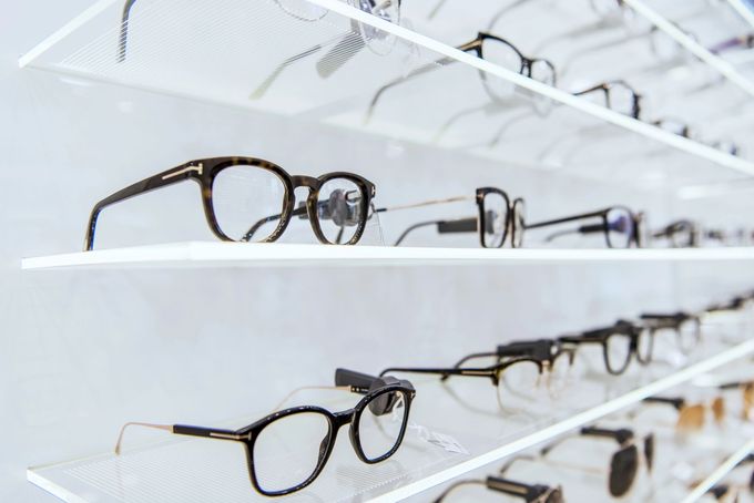 Montature per occhiali esposte su scaffali bianchi in un negozio di ottica.
