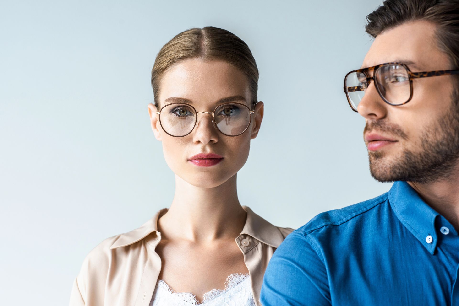 Due persone con gli occhiali in un ritratto in studio, una donna di fronte e un uomo con una camicia blu di profilo.