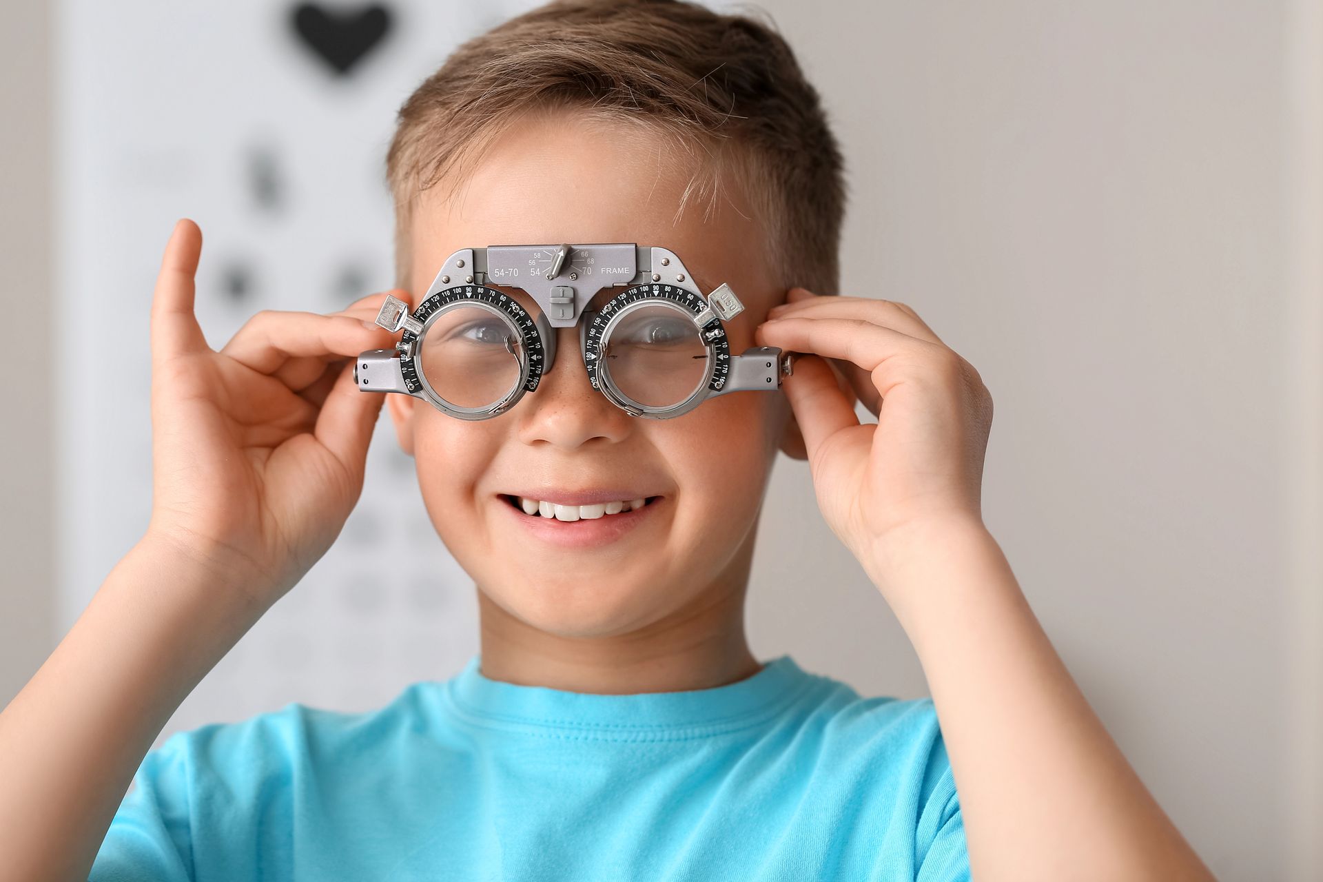 Bambino sorridente che tiene degli occhiali stravaganti davanti al viso, su uno sfondo chiaro.