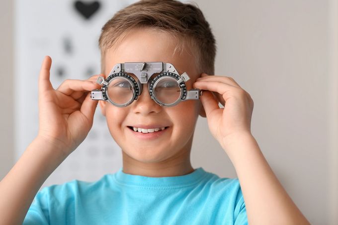 Bambino sorridente che tiene degli occhiali stravaganti davanti al viso, su uno sfondo chiaro.