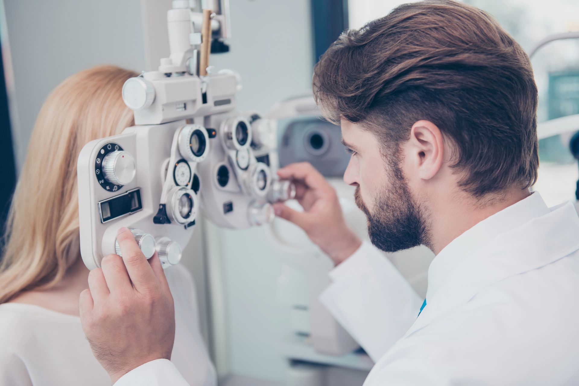 L'optometrista regola un forottero per esami della vista mentre il paziente è seduto durante un test della vista.