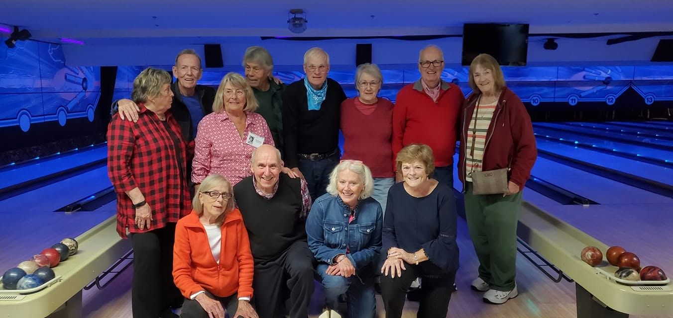 Group posing at a bowling alley, with lanes and bowling balls in the background.