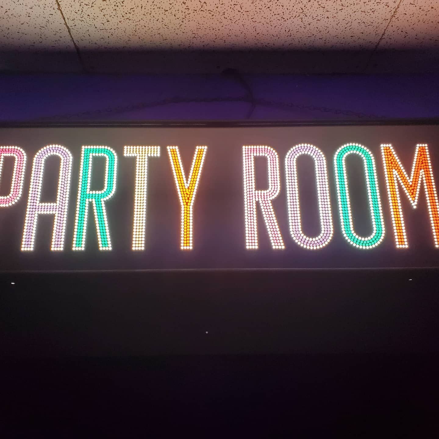 Neon sign reading “PARTY ROOM” in pink and teal on a dark wall