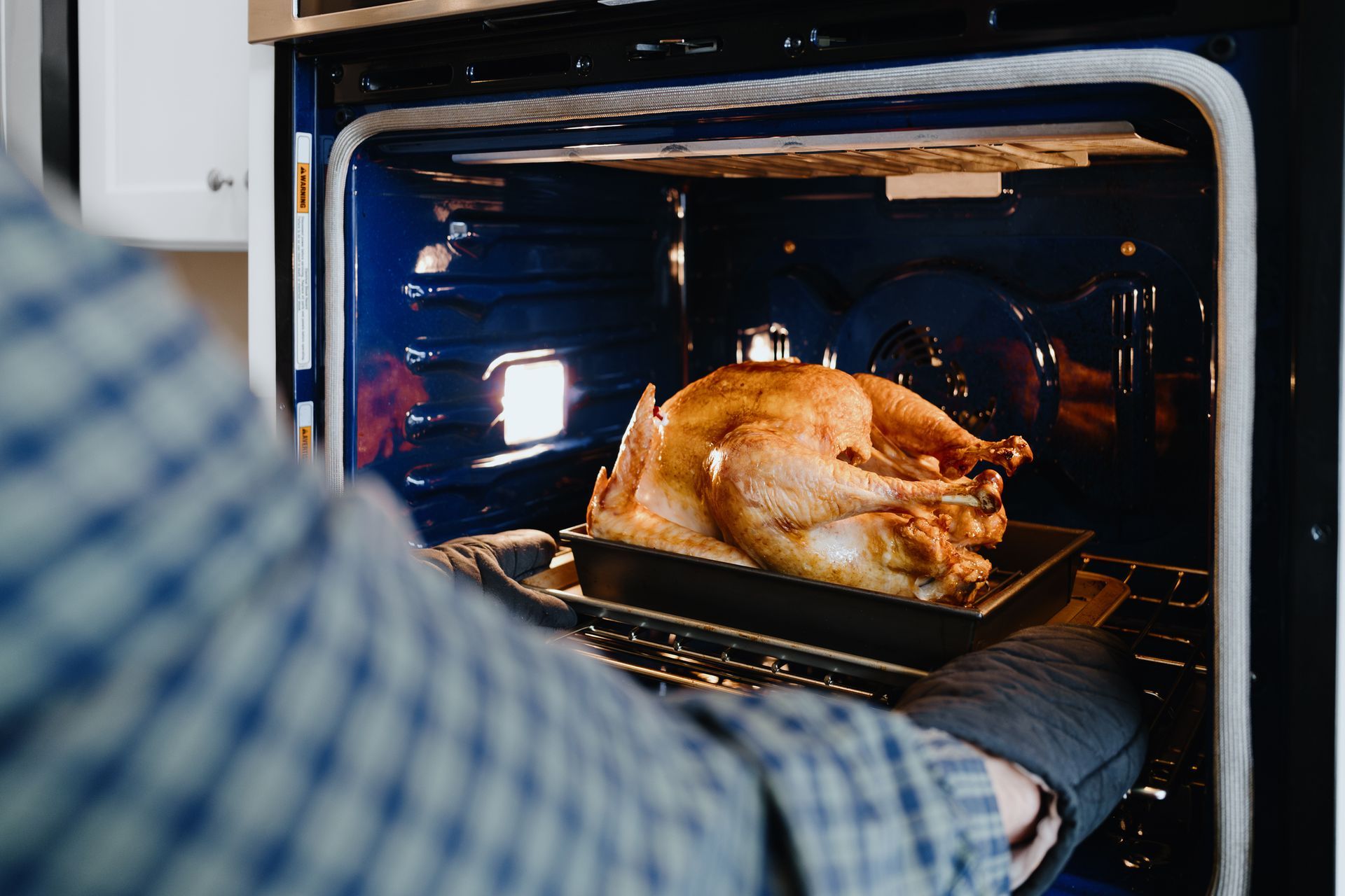 Person placing roasted turkey in a hot oven, wearing oven mitts. Person placing roasted turkey in a hot oven, wearing oven mitts.