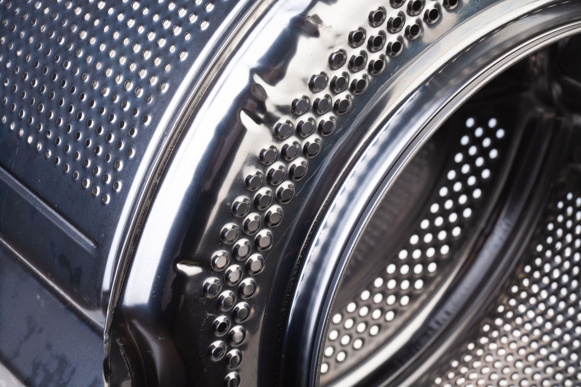 Close-up view of a stainless steel washing machine drum with numerous small holes. Close-up view of a stainless steel washing machine drum with numerous small holes.