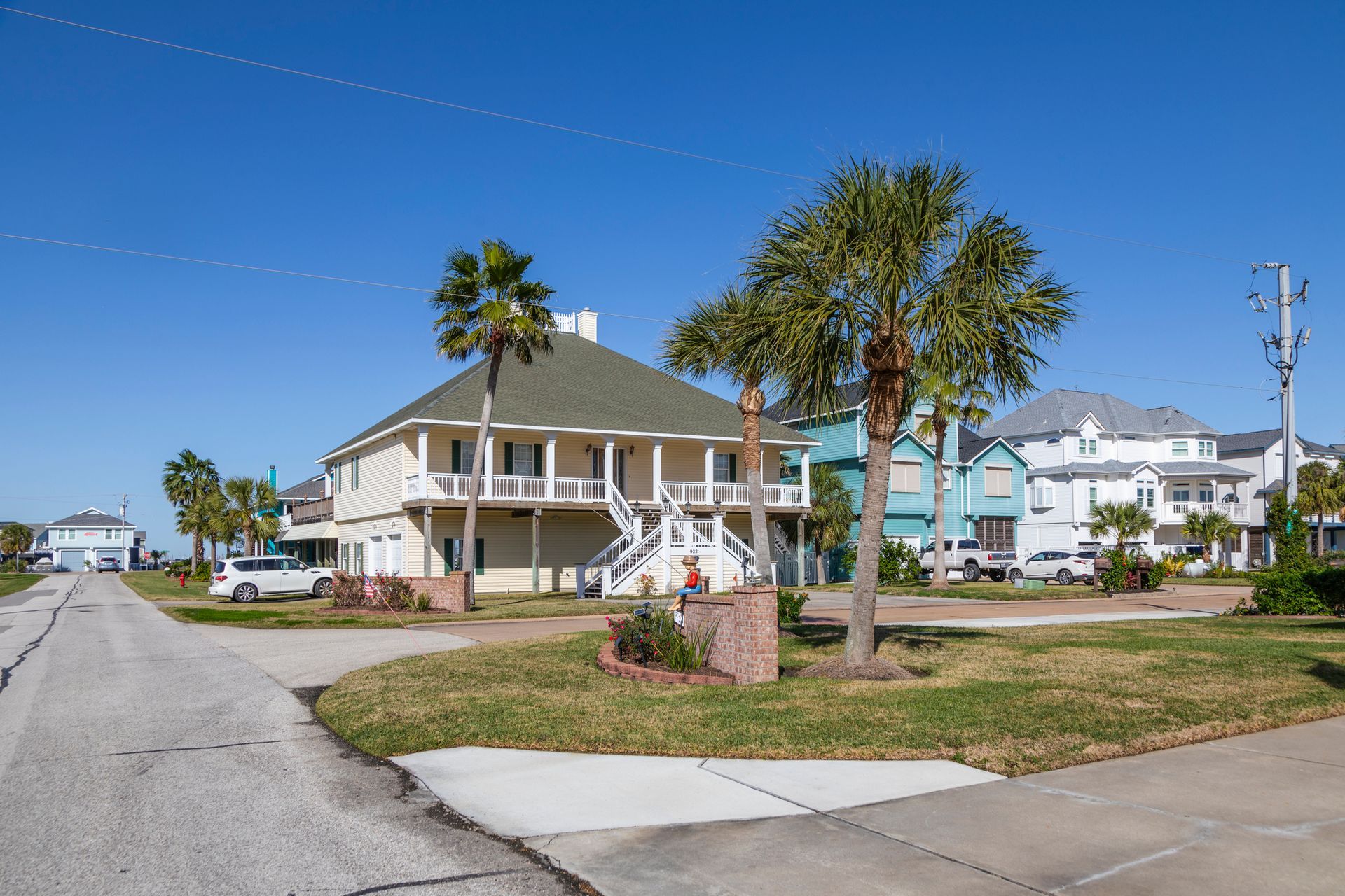 Beachfront houses along a residential street on a sunny day. Palm trees and blue sky.