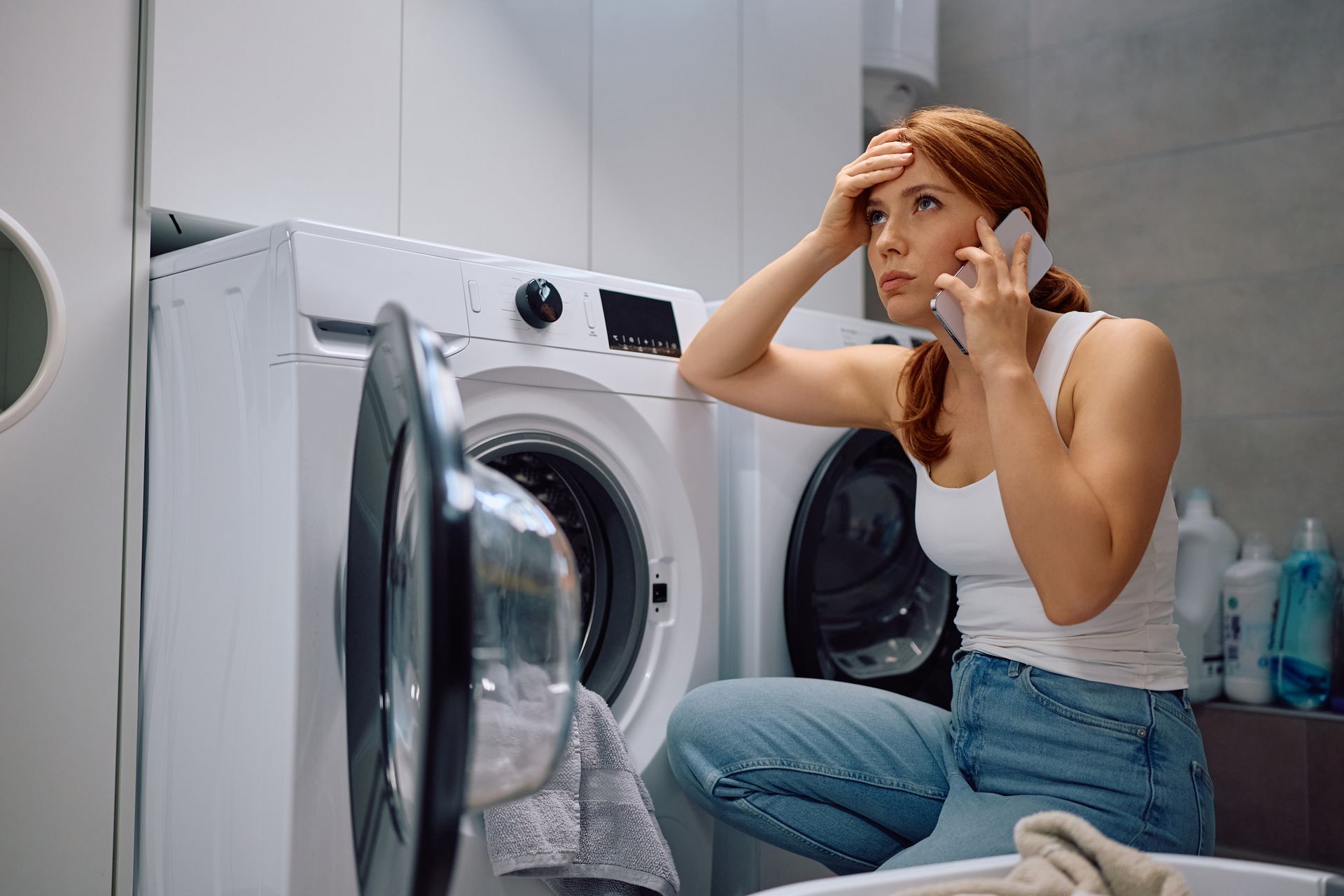Woman on phone, distressed, next to washing machine with open door, indoor setting. Woman on phone, distressed, next to washing machine with open door, indoor setting.