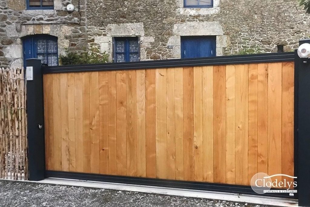 Patio d'une maison moderne avec table noire, grande façade crème et volets sombres ouverts sous un toit de tuiles