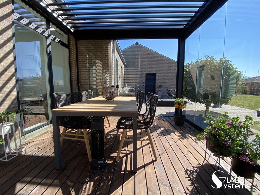Terrasse extérieure couverte avec table à manger en bois, chaises noires, plantes en pot et vue sur le jardin.