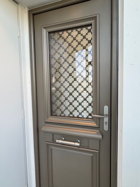 Porte extérieure en métal gris avec vitrage dépoli décoratif et poignée argentée.