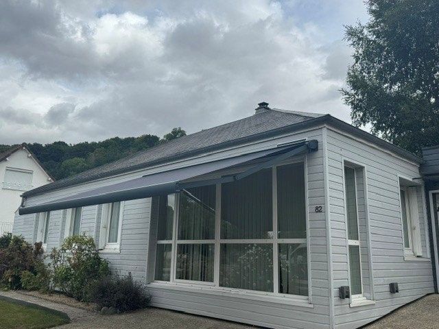 Patio couvert avec auvent blanc, sièges extérieurs et pelouse verte à côté d'une maison moderne
