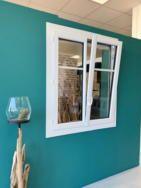Fenêtre à cadre blanc encastrée dans un mur bleu sarcelle, à côté d'un bougeoir décoratif en verre posé sur un support en bois flotté.
