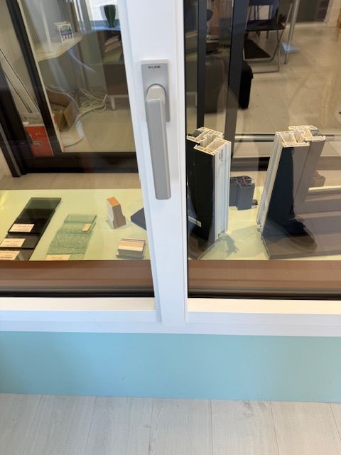 Vitrine en verre présentant des échantillons et de la quincaillerie de porte sur des étagères derrière un cadre blanc.