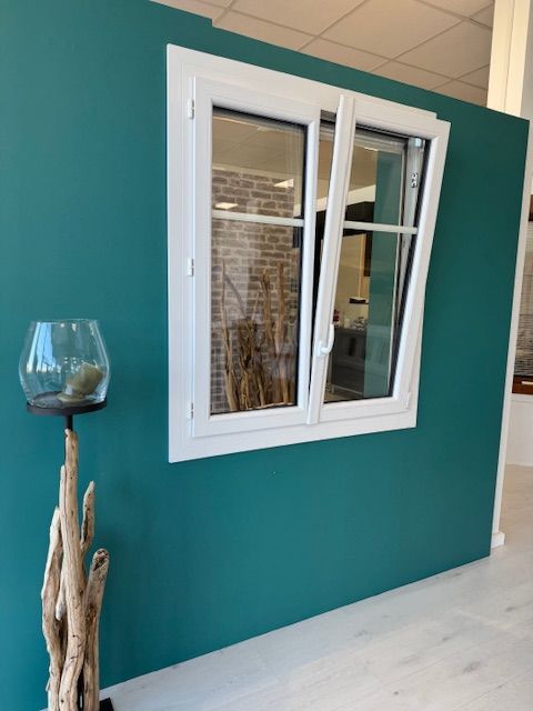 Fenêtre à cadre blanc dans un mur intérieur bleu sarcelle, à côté d'un morceau de bois flotté décoratif et d'un bol en verre sur un support.