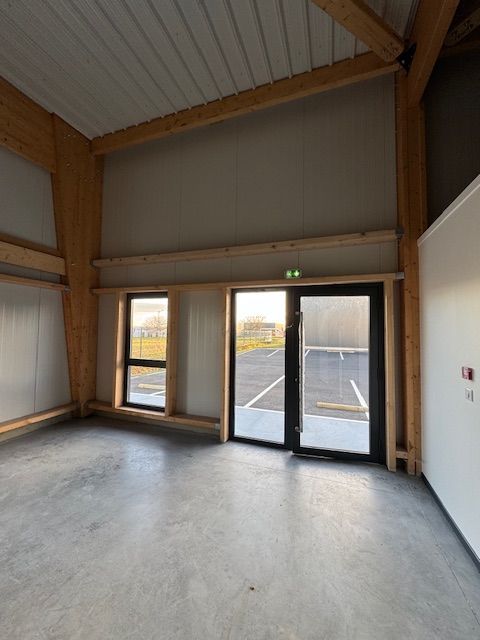 Pièce moderne vide avec sol en béton, poutres en bois et double porte vitrée donnant sur l'extérieur