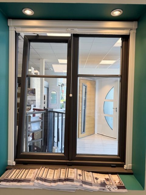 Petite fenêtre en verre à cadre noir dans un mur turquoise, donnant sur un couloir intérieur éclairé.