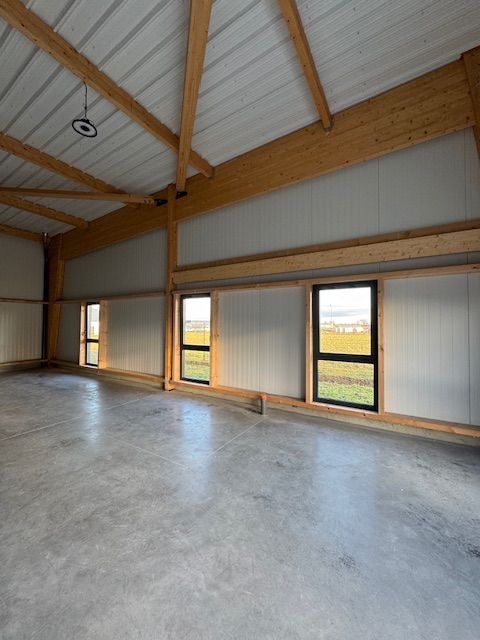 Intérieur vide de style industriel avec sol en béton, poutres en bois apparentes et hautes fenêtres.