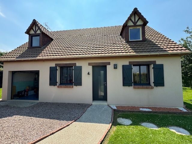 Maison de plain-pied couleur crème avec toit foncé, lucarnes, porte d'entrée, garage et jardin paysager.