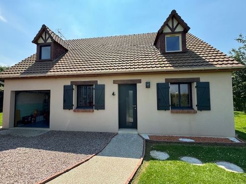 Maison de plain-pied couleur crème avec toit marron, volets foncés, garage et allée d'entrée.