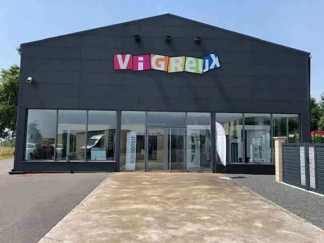 Vue de face d'un magasin gris foncé avec une enseigne colorée « VIGREUX » et une entrée vitrée.