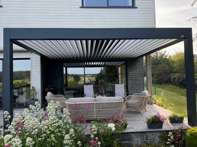 Patio moderne avec pergola noire, sièges en osier et plantes fleuries à l'extérieur d'une maison