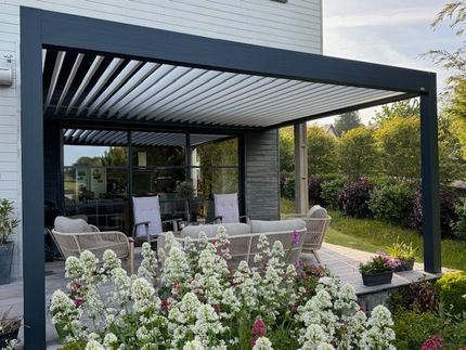 Terrasse arrière avec pergola noire, sièges d'extérieur et plantes fleuries à côté d'une maison moderne