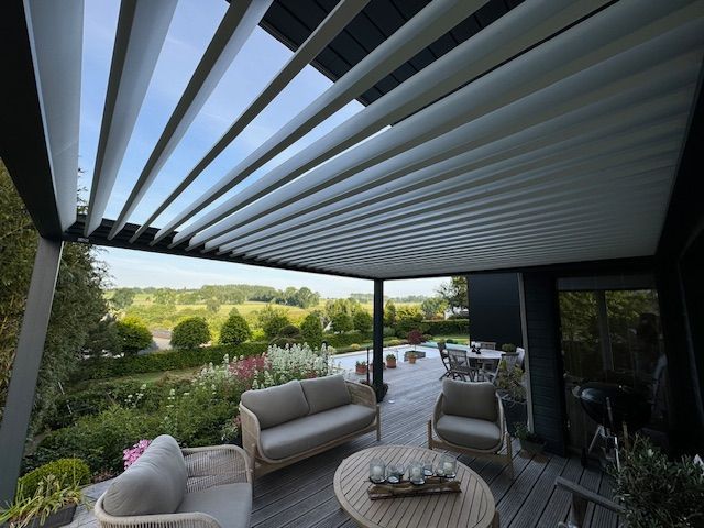 Terrasse couverte avec chaises longues blanches, table basse et toit rétractable donnant sur un jardin verdoyant.