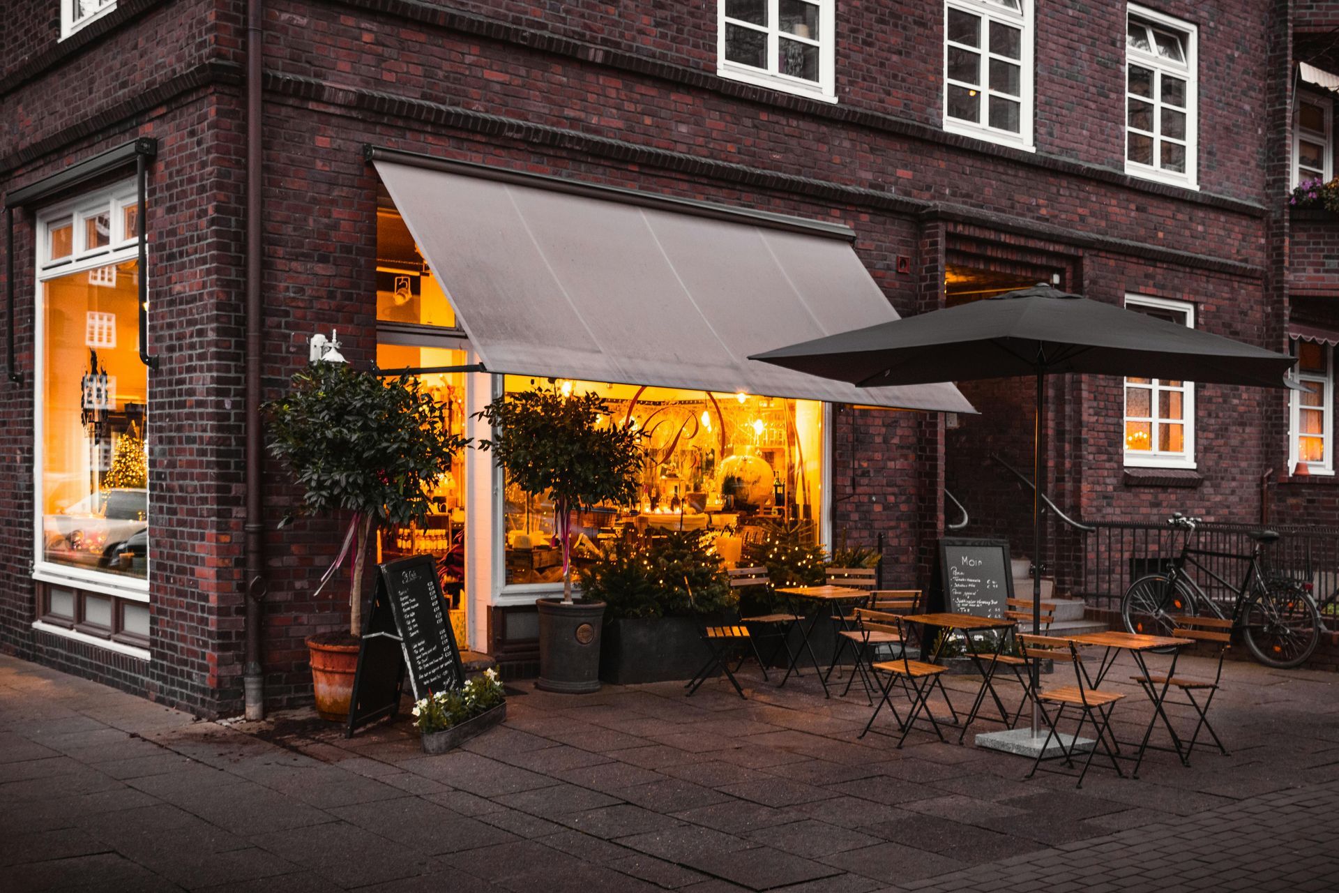 Café de rue avec éclairage intérieur chaleureux, auvents et tables en terrasse à côté d'un bâtiment en briques.