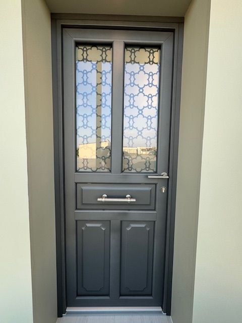 Porte d'entrée gris foncé avec panneaux de verre décoratifs et fente à lettres dans une entrée en retrait