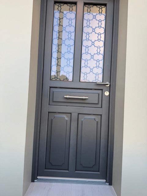 Porte d'entrée gris foncé avec panneaux de verre décoratifs et fente à lettres dans un mur blanc.