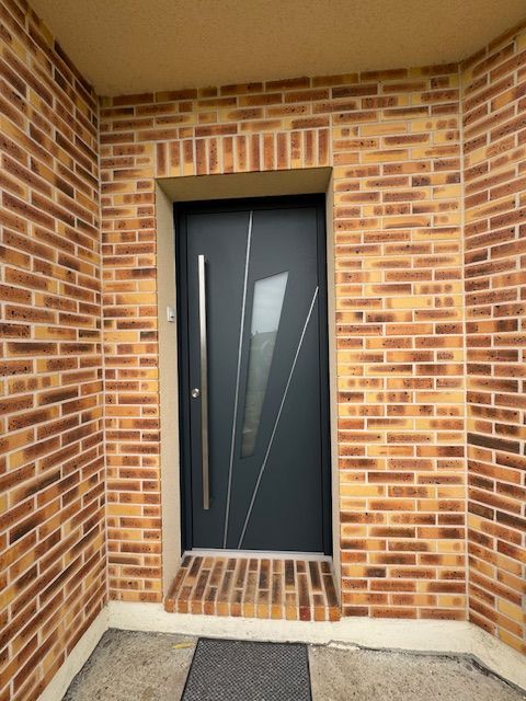 Entrée en briques avec une porte d'entrée moderne sombre et une petite marche.